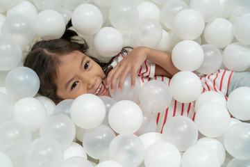 Fototapeta na wymiar Happy cute asian child girl having fun to play with white plastic balls in the playground