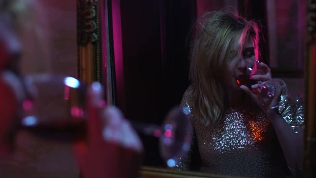 Woman drinking wine in front of nightclub mirror, lifestyle, alcohol addiction