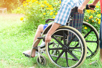 Paralyzed man using wheelchair during walk in park. He holds his hands on the wheel.