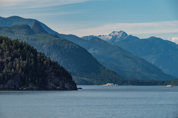 layers of forest covered mountains on the island over the horizon of the ocean under cloudy blue sky