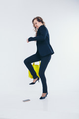 girl puts a foot on the phone. the heel breaks a smartphone. Businesswoman went crazy. Close up on white background. yellow bag
