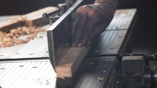 A carpenter's hands holding a piece of wood and using jointer power machine