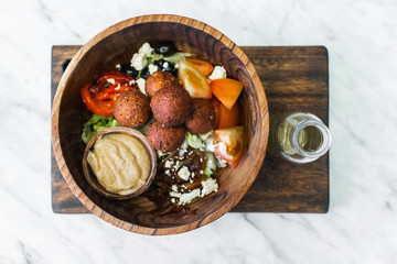 Wooden bowl with falafel balls, hummus and fresh salad. Olive oil in bottle on side. White marble background, top view. Traditional arabic eastern food. Veganism concept.
