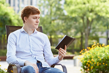 Young attractive man in white shirt sitting on brown chair in the park on green background - 279738150