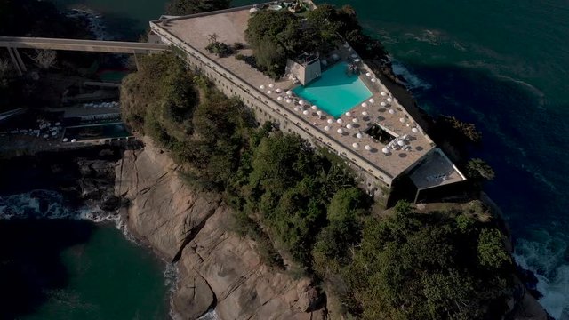 Aerial view of rooftop swimming pool with beach umbrellas revealing the island the construction is build on and the wider coastal seascape of Rio de Janeiro