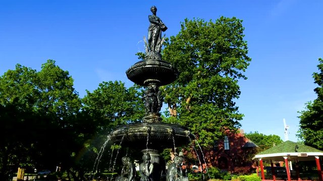 A historic refurbished fountain in the middle of a city park in the daytime with a misty rainbow.