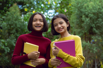 Two happy young Asian girls hold note book  with green background.