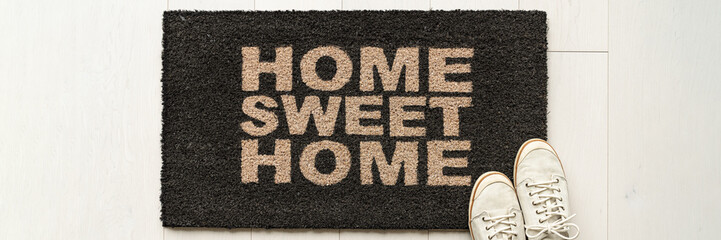 Home condo door mat sweet home doormat text at condo entrance with casual shoes panoramic banner. House move in concept.