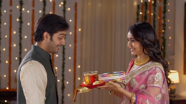 Newly married couple celebrating their first Karwa Chauth together - Indian festival. Young beautiful wife performing Karwa Chauth traditions with her husband  praying for his long and safe life in...