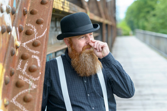 Bearded man standing outdoors rubbing his nose