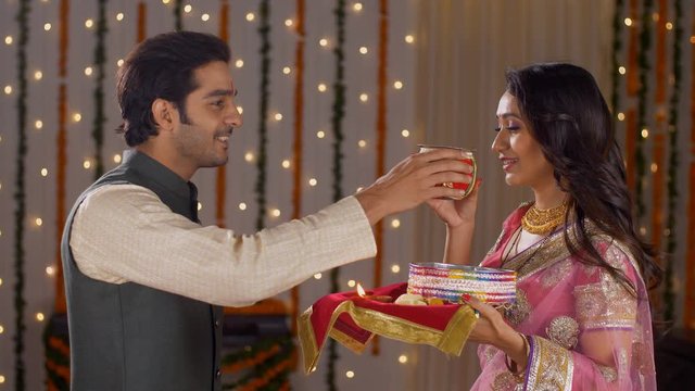 Newly wed couple celebrating their first Karwa Chauth together - Indian festival. Good looking husband performing Karwa Chauth traditions of offering water to her fasting wife in traditional wear -...