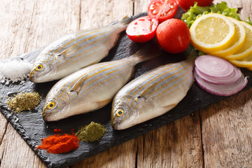 Healthy raw Sarpa salpa with fresh vegetables and spices close-up on a slate board. horizontal