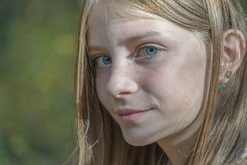 Naklejka premium Beautiful blonde young girl with freckles outdoors on nature background in autumn, close up portrait