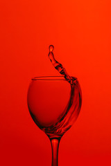 splash of water in wineglass isolated on red background.