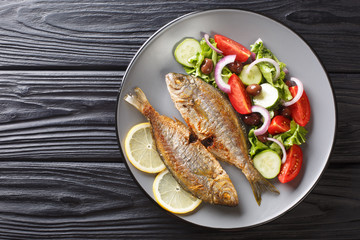fresh fried Sarpa salpa fish with summer vegetable salad  and lemon close-up on a plate. Horizontal top view