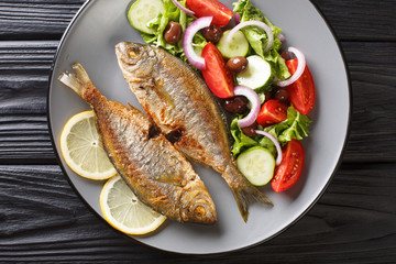 fried Salema porgy sea fish with fresh vegetable salad close-up on a plate on the table. Horizontal top view