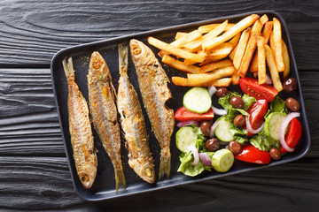 Fresh fried boops boops fish with summer vegetable salad and french fries close-up on a plate. horizontal top view