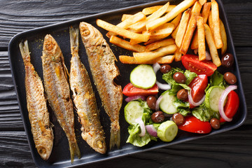 Fried Mediterranean Boops boops fish served with fresh salad and french fries close-up on a plate. Horizontal top view