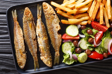 Fried boops boops fish with fresh vegetable salad and french fries close-up on a plate. horizontal top view