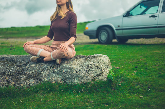 Young woman in meditation pose by her car