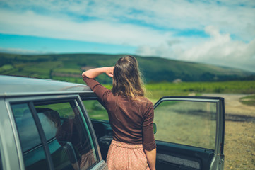 Young woman relaxing by her car on the moor in summer