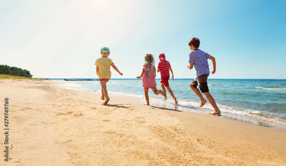 Wall mural Happy kids on vacations at seaside running in the water