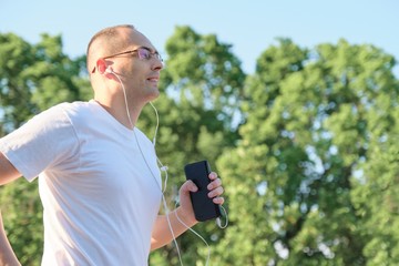 Middle aged male with glasses runs through city park with headphones