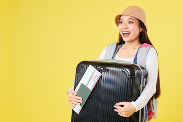 Happy excited young Vietnamese woman holding her baggage, international passport and ticket