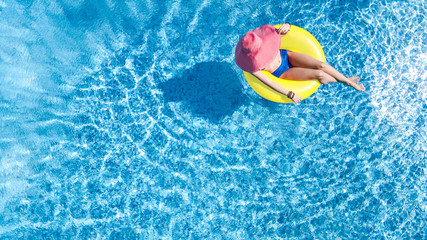 Beautiful young woman in hat in swimming pool aerial top view from above, young girl in bikini relaxes and swims on inflatable ring donut and has fun in water on family vacation, tropical holiday reso