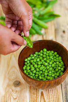 closeup of woman hand depod green peas in brown dish, on wooden table.