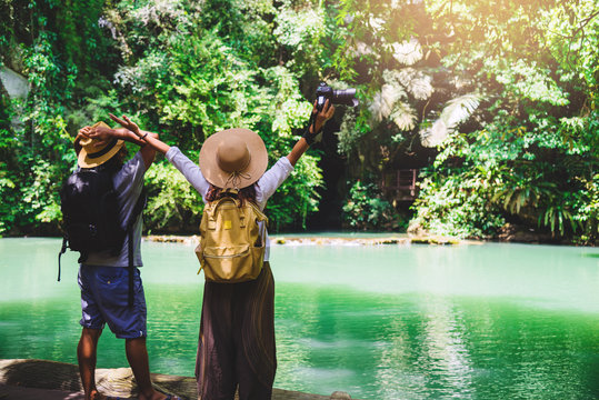 Couple travelers with backpacks relaxing in greens jungle and enjoying view in waterfall. Tourism hiking nature study. Couples traveling taking pictures of nature on holiday.