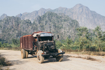 Old truck driving on the dirt road with Zwegabin mountain on background in Hpa-An, Myanmar