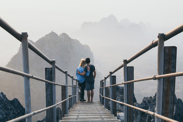 Young couple standing on mountain peak with stairs going down during sunrise foggy morning in Hpa-An, Myanmar