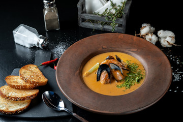 Spicy soup of mashed potatoes with mussels from the pumpkin with greens. Beautifully served table.