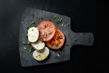 Tomato and mozzarella with basil leaves on a black slate.