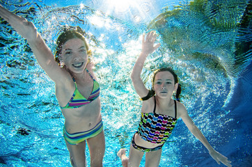 Children swim underwater in swimming pool, happy active girls have fun under water, kids fitness and sport on active family vacation