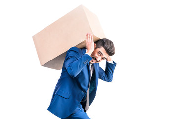 Attractive young man in a blue suit carries a cardboard box on his back. Isolated.