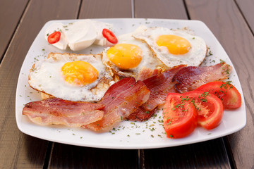 Healthy bacon fried egg on toast bread breakfast on plate , fresh tomatoes and cheese on plate , wood background.
