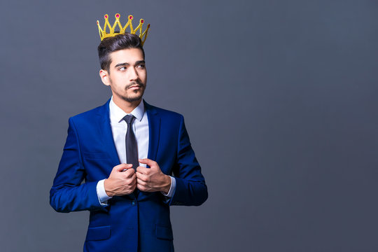 A young man with a crown on his head on a gray background looks to the side