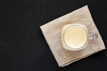 Peanut butter banana smoothie in a glass jar on a black surface, top view. Flat lay, from above, overhead.
