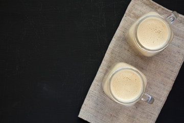 Peanut butter banana smoothie in glass jar mugs on a black background, top view. Flat lay, from above, overhead. Copy space.