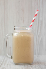 Peanut butter banana smoothie in a glass jar on a white wooden background, side view. Close-up.