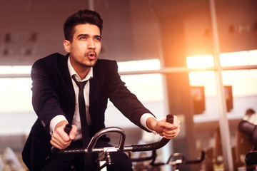 Young guy in a white shirt and suit on a stationary bike in the gym.