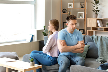 Young offended couple after quarrel sitting on sofa at home