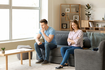 Young offended couple after quarrel sitting on sofa at home