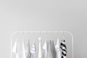 Stylish kid clothes hanging on rack against light background
