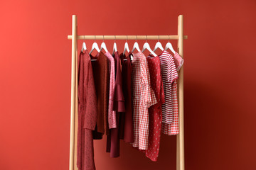 Rack with hanging clothes on color background