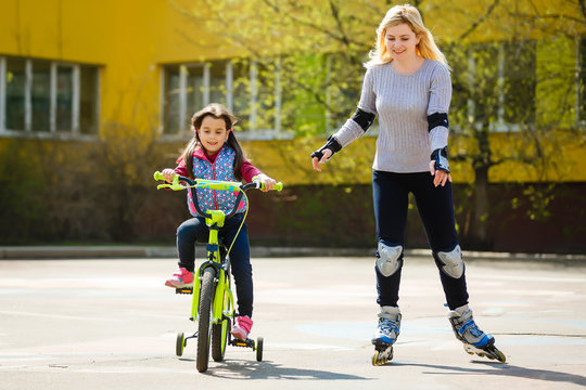 A young mother roller skating. Daughter riding a bicycle