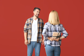 Wife hiding gift for her husband behind back on color background