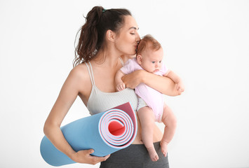 Mother with yoga mat and cute little baby on white background